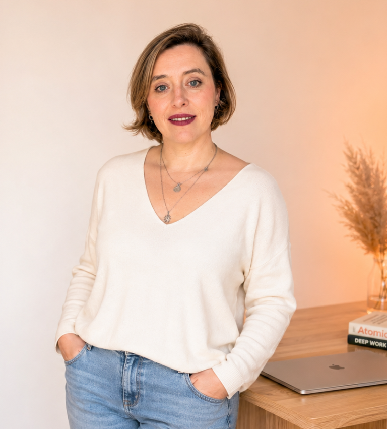 Inhaberin Manuela Guerinaud-Klein mit kurzem Haar trägt einen weißen Pullover und steht vor einem Holztisch.